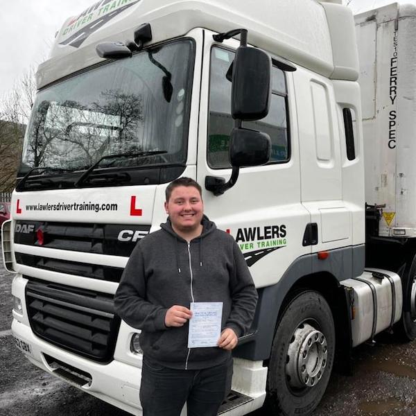 Newly qualified HGV Class 1 category C+E driver holding pass certificate in front of HGV truck