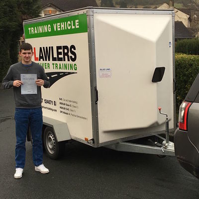 Newly qualified trailer towing driver holding b+e pass certificate in front of  trailer training vehicle
