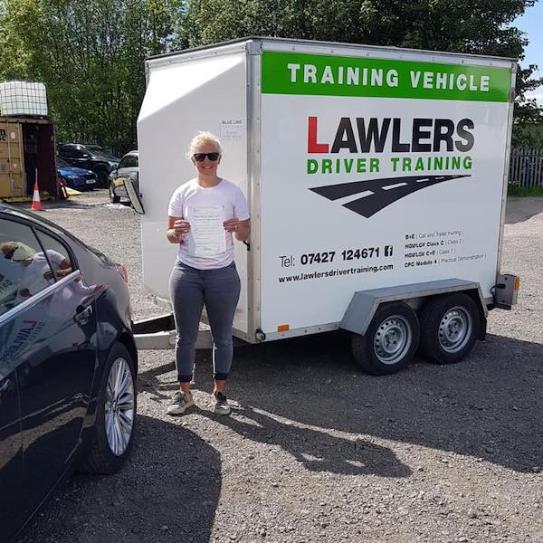 Newly qualified trailer towing lady driver holding b+e pass certificate in front of  trailer training vehicle