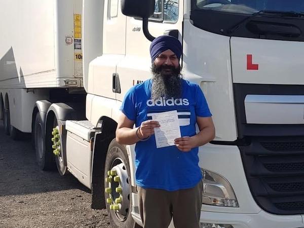 Newly qualified zero faults HGV Class 1 category C+E driver holding pass certificate in front of HGV truck