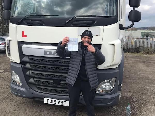 Newly qualified HGV Class 1 driver pointing to pass certificate in front of HGV Category C+E truck