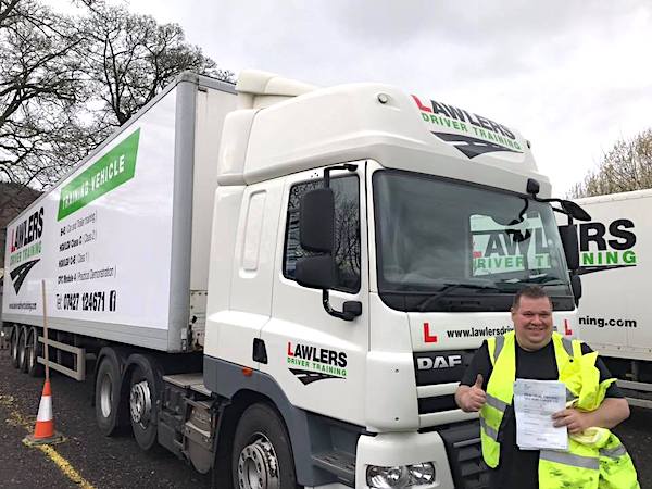 Newly qualified class 1 artic with trailer category c + e  hgv driver holding pass certificate in front of HGV truck