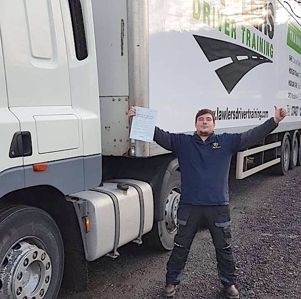 Newly qualified class 1 artic with trailer category c + e  hgv driver with arms up holding pass certificate in front of HGV truck