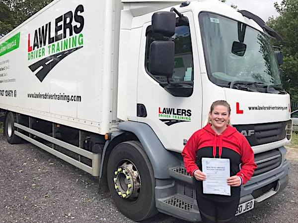 Newly qualified female HGV Class 2 category C driver holding pass certificate in front of HGV truck