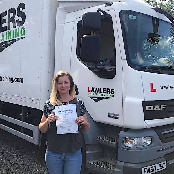 Newly qualified lady HGV Class 2 category C driver holding pass certificate in front of HGV truck