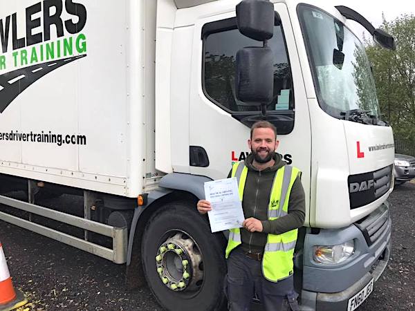 Newly qualified HGV Class 2 category C driver holding pass certificate in front of HGV truck