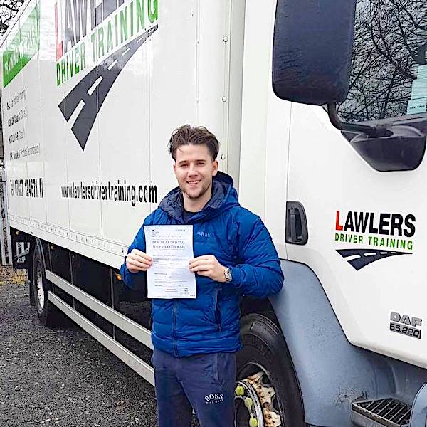 Newly qualified HGV Class 2 category C driver holding pass certificate in front of HGV truck