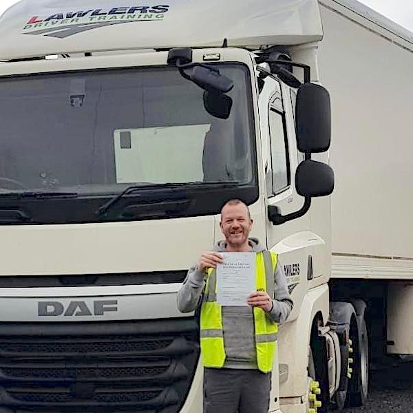 Newly qualified HGV Class 1 driver holding pass certificate in front of HGV category C+E truck