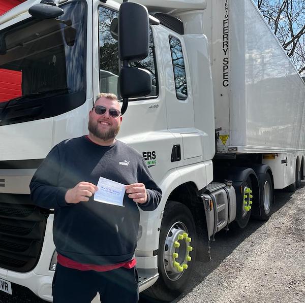 Newly qualified HGV Class 1 driver holding pass certificate in front of HGV category C+E truck