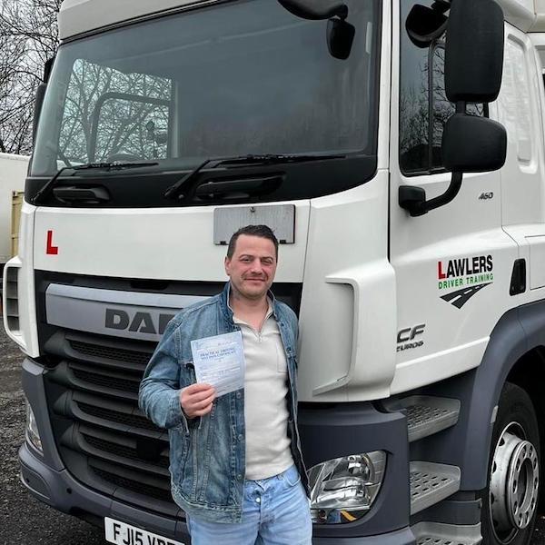 Newly qualified HGV Class 1 category C+E driver holding pass certificate in front of HGV truck