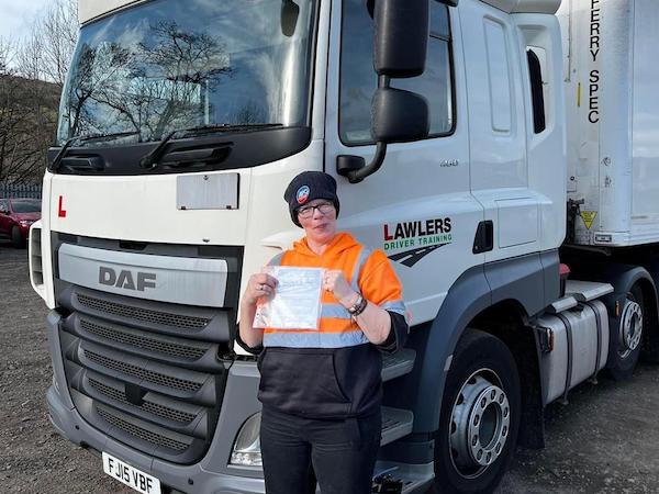 Newly qualified female HGV Class 1 category C + E driver holding pass certificate in front of HGV truck