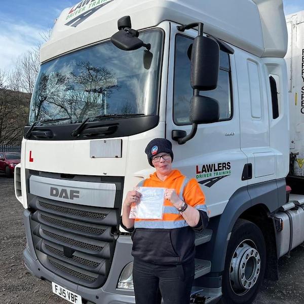 Newly qualified lady HGV Class 1 driver holding pass certificate in front of HGV category C+E truck