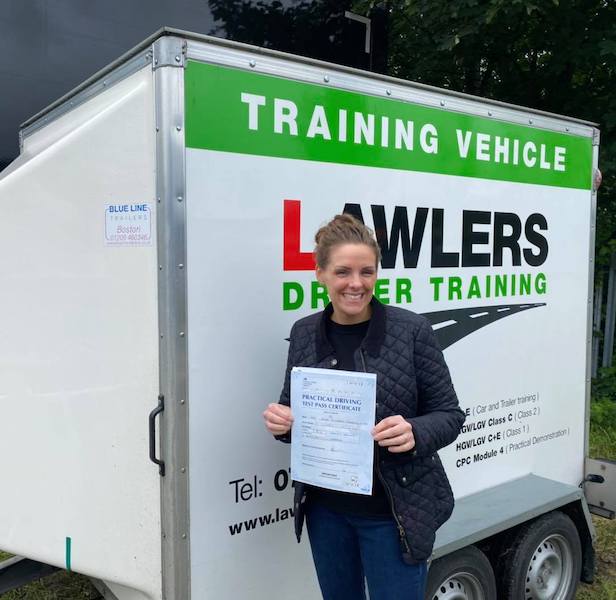Newly qualified lady trailer towing driver holding b+e pass certificate in front of  trailer training vehicle