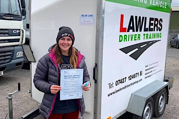 Newly qualified trailer towing female driver holding b+e pass certificate in front of  trailer training vehicle
