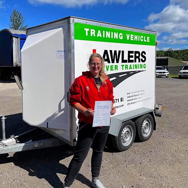Newly qualified trailer towing lady driver holding b+e pass certificate in front of  trailer training vehicle