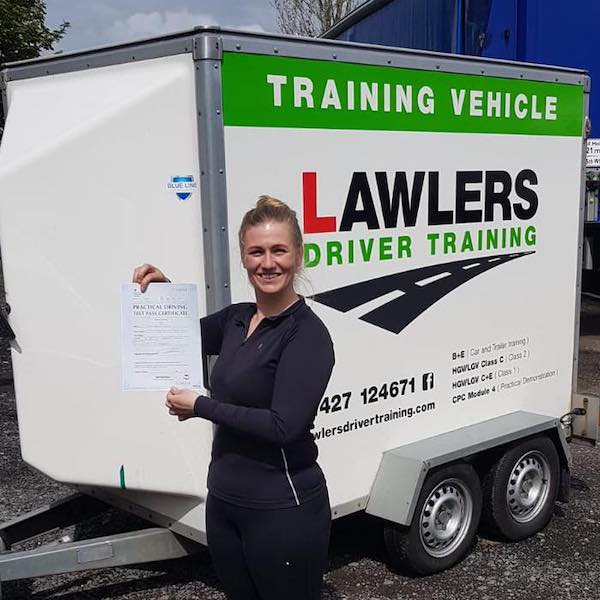 Newly qualified female trailer towing driver holding b+e pass certificate in front of  trailer training vehicle