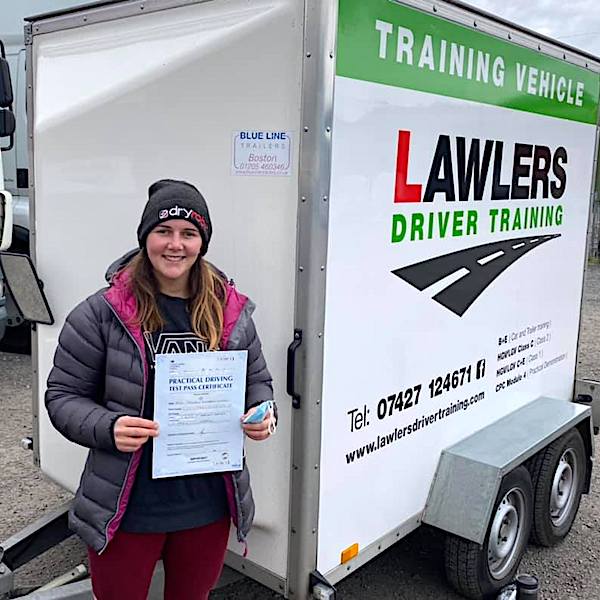 Newly qualified female trailer towing driver holding b+e pass certificate in front of  trailer training vehicle